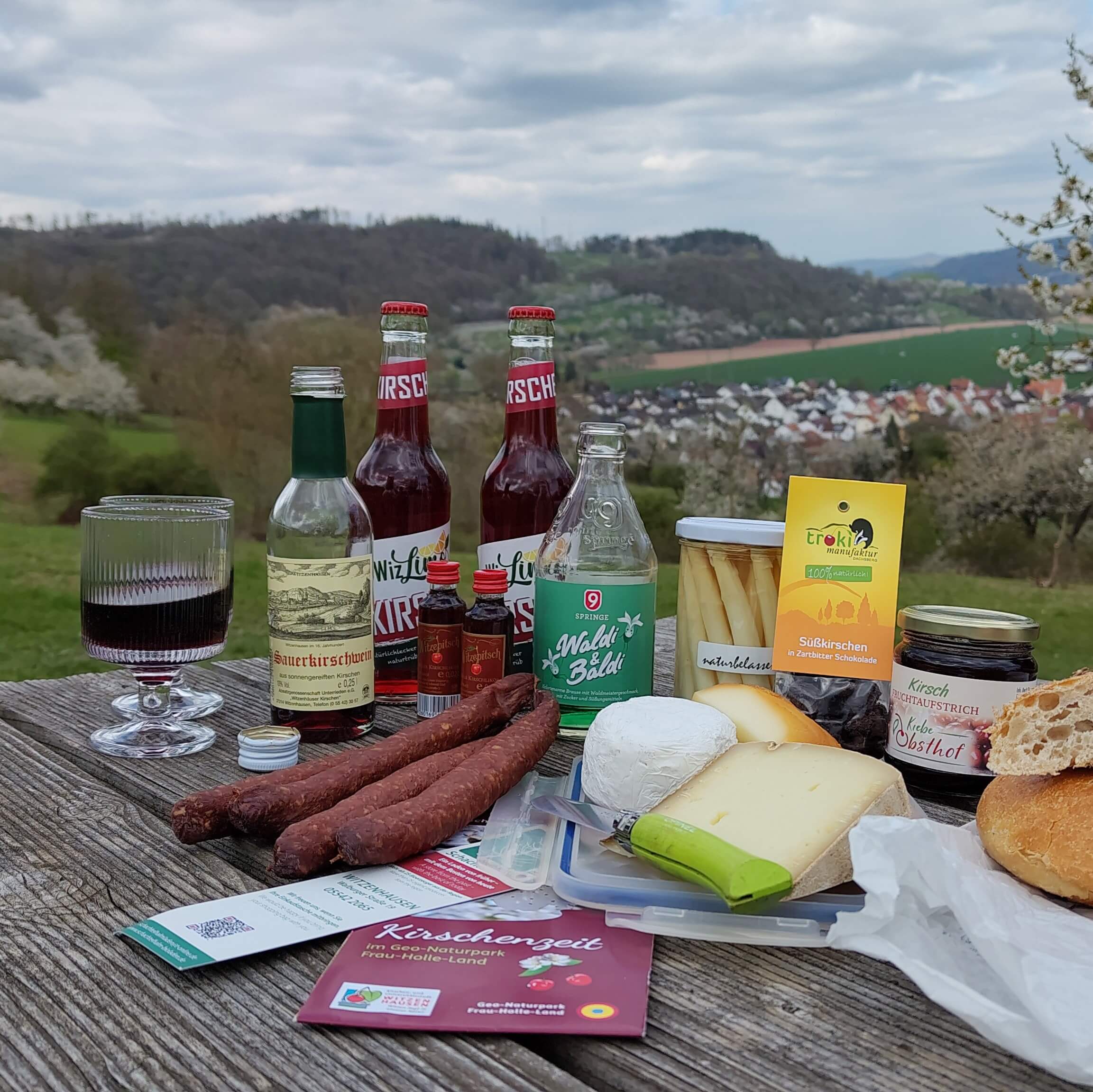 Picknick mit regionalen Produkten wie Wurst, Käse, Kirschwein, Limonade, Konfitüre und eingelegtem Gemüse.