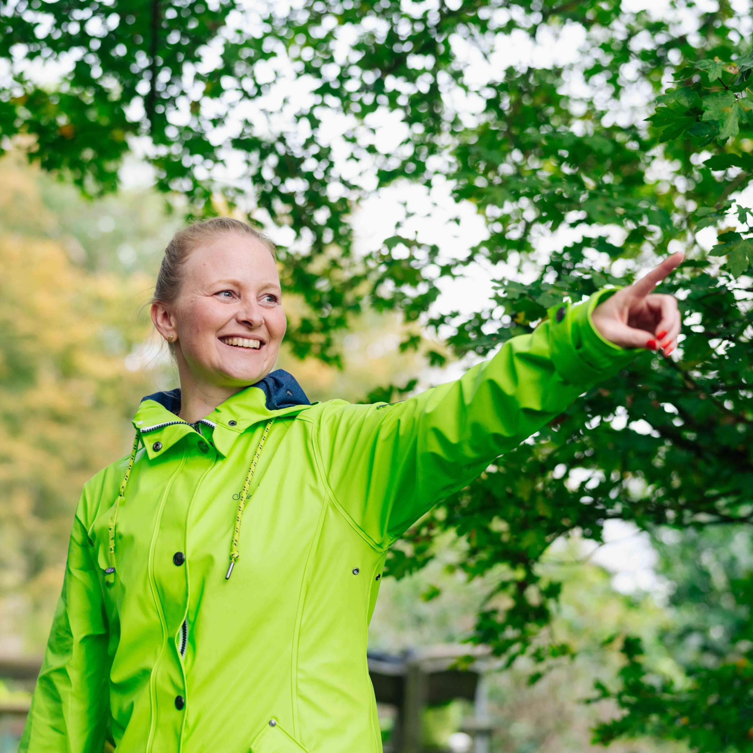 Julia Friedrich zeigt lächelnd nach rechts in die Landschaft.