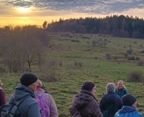 Mehrere Menschen vor einer winterlich kargen Landschaft. Im Hintergrund ein Sonnenuntergang.