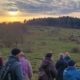 Mehrere Menschen vor einer winterlich kargen Landschaft. Im Hintergrund ein Sonnenuntergang.