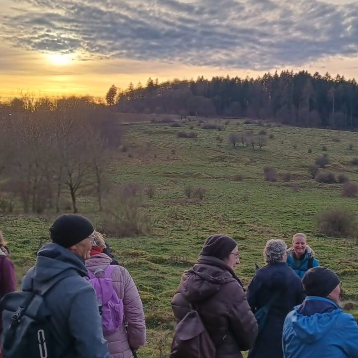 Mehrere Menschen vor einer winterlich kargen Landschaft. Im Hintergrund ein Sonnenuntergang.